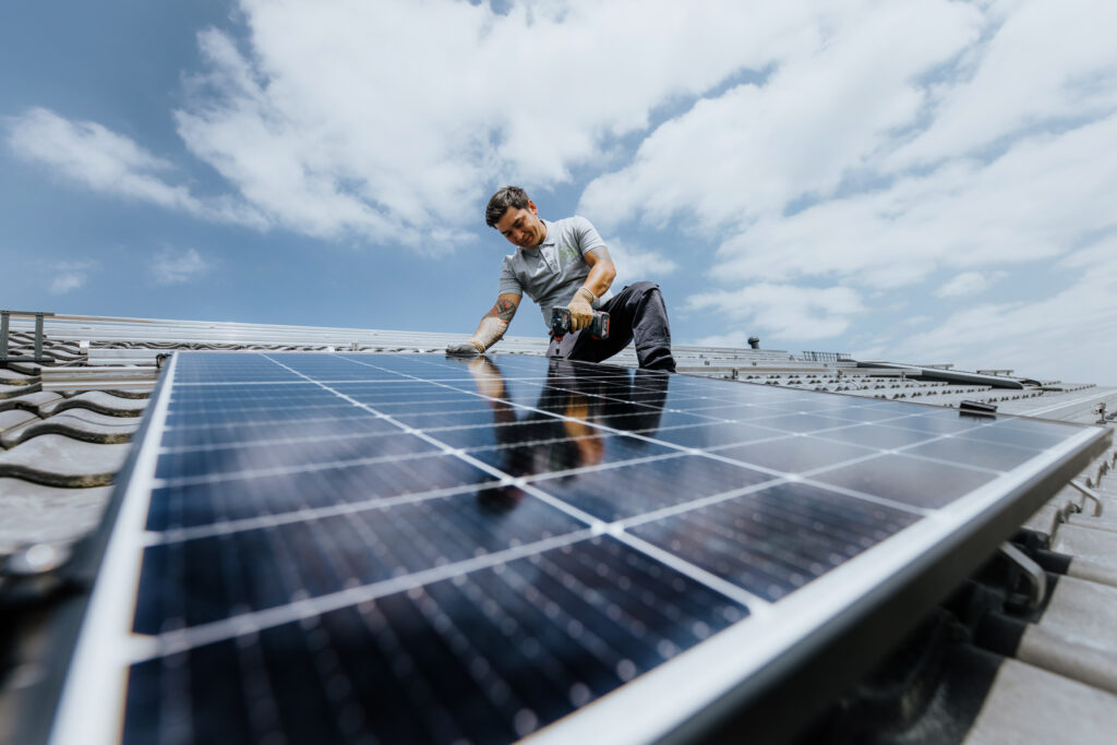 Eine Person auf einem Hausdach montiert ein PV-Modul. 